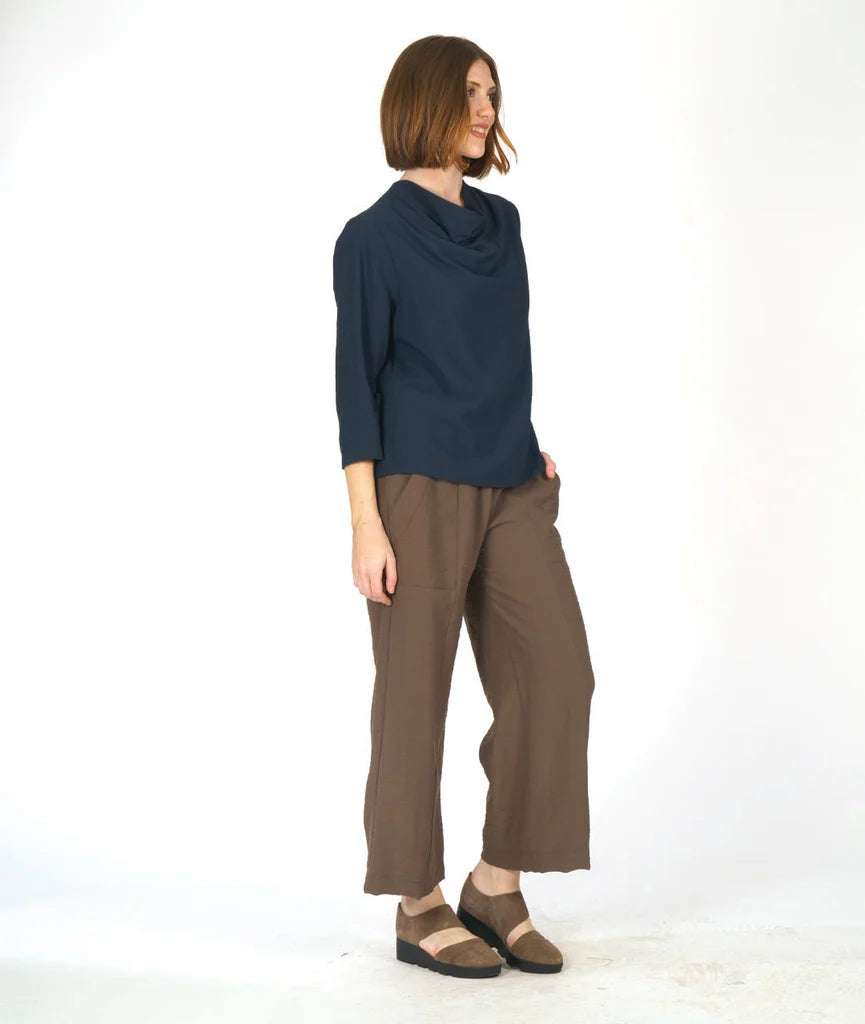 model wearing a navy blue cowl top and brown pants against a white background