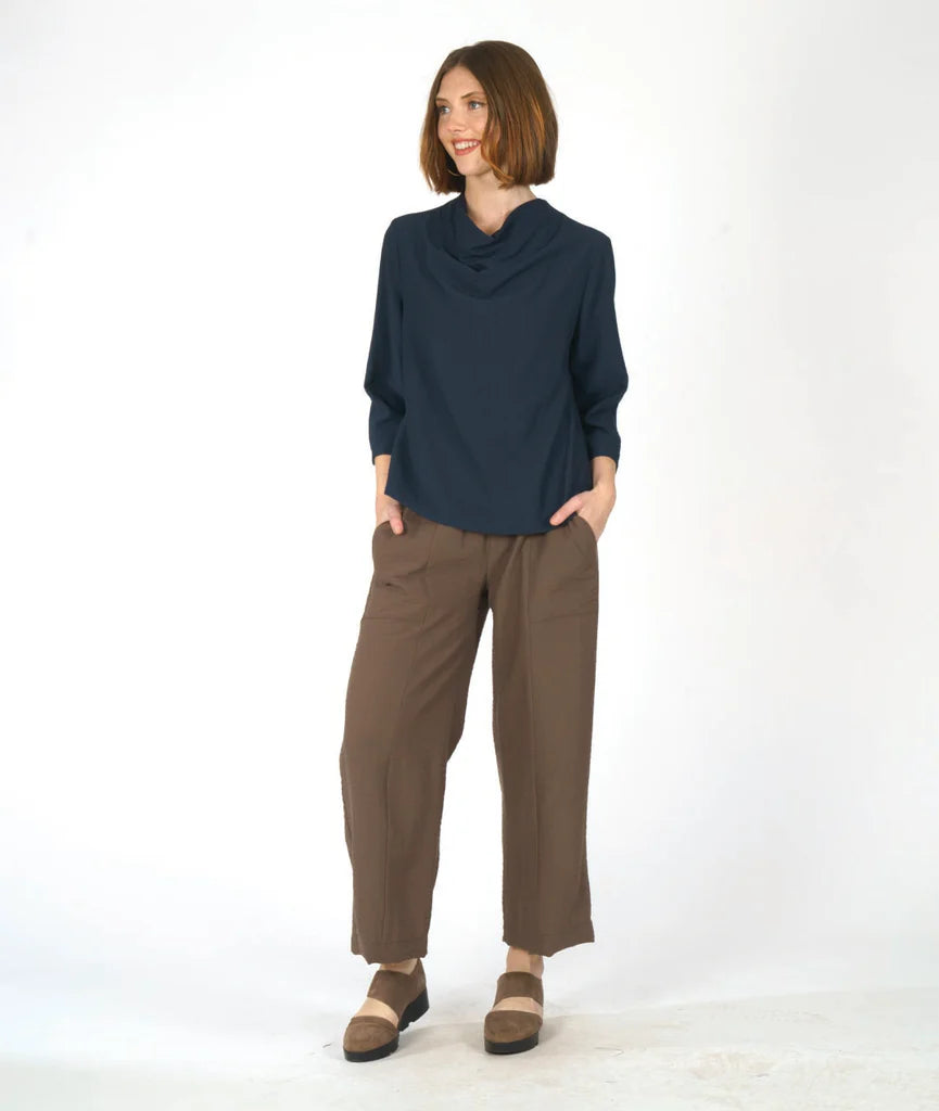 model wearing a navy blue cowl top and brown pants against a white background