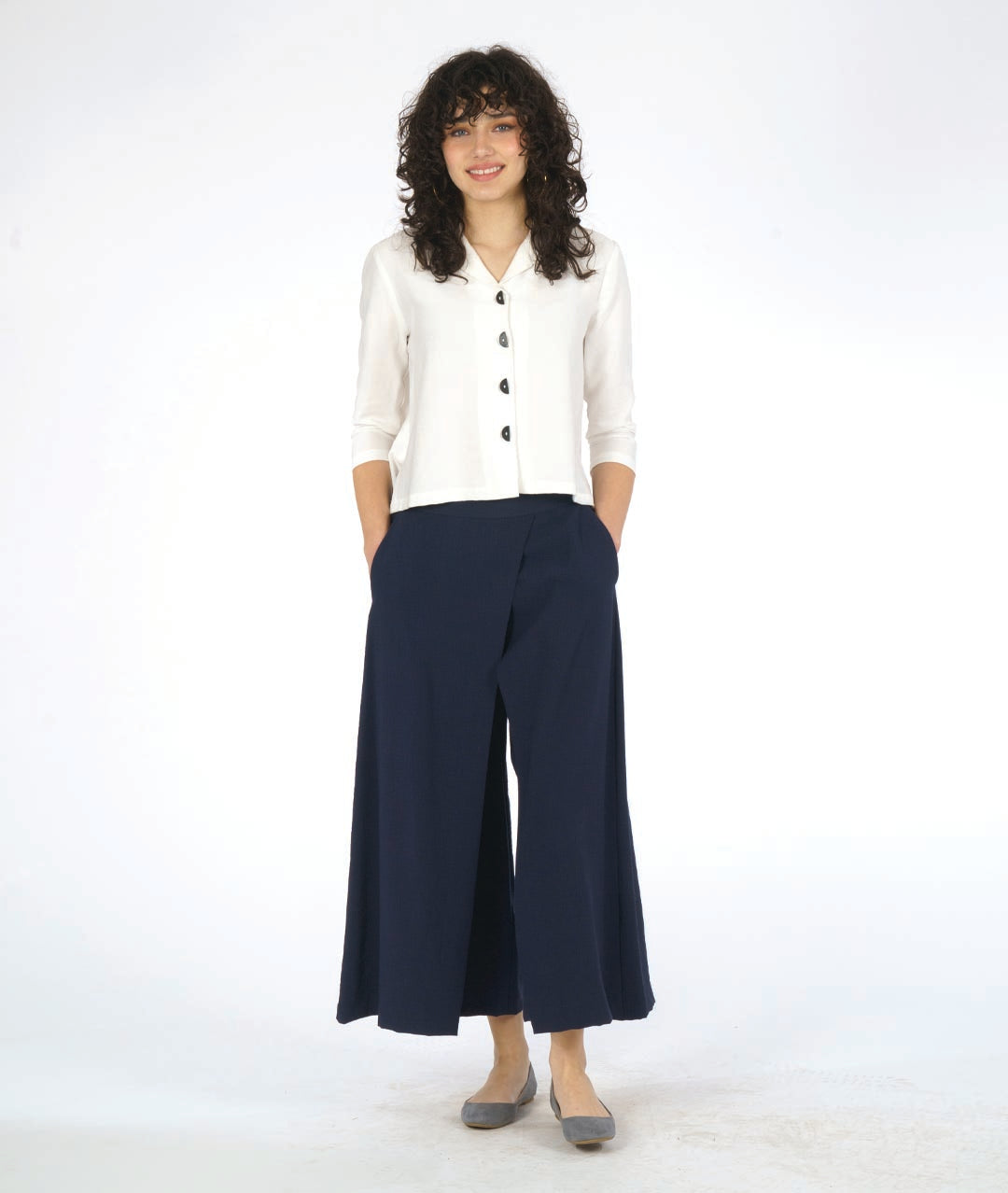 model in a short white button down blouse with a 3/4 sleeve and half moon buttons. worn with a navy blue wide leg pant with overlapping panels in the front
