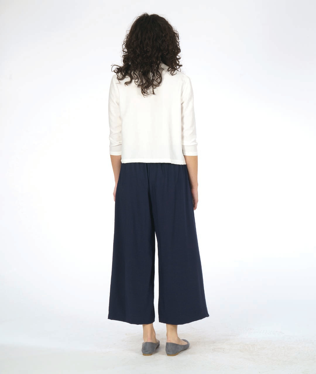 model in a short white button down blouse with a 3/4 sleeve and half moon buttons. worn with a navy blue wide leg pant with overlapping panels in the front