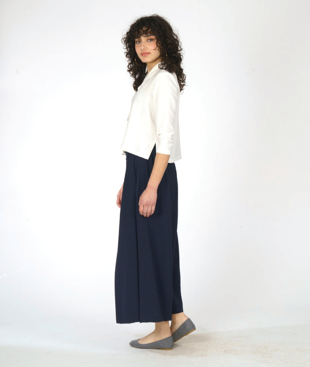 model in a short white button down blouse with a 3/4 sleeve and half moon buttons. worn with a navy blue wide leg pant with overlapping panels in the front