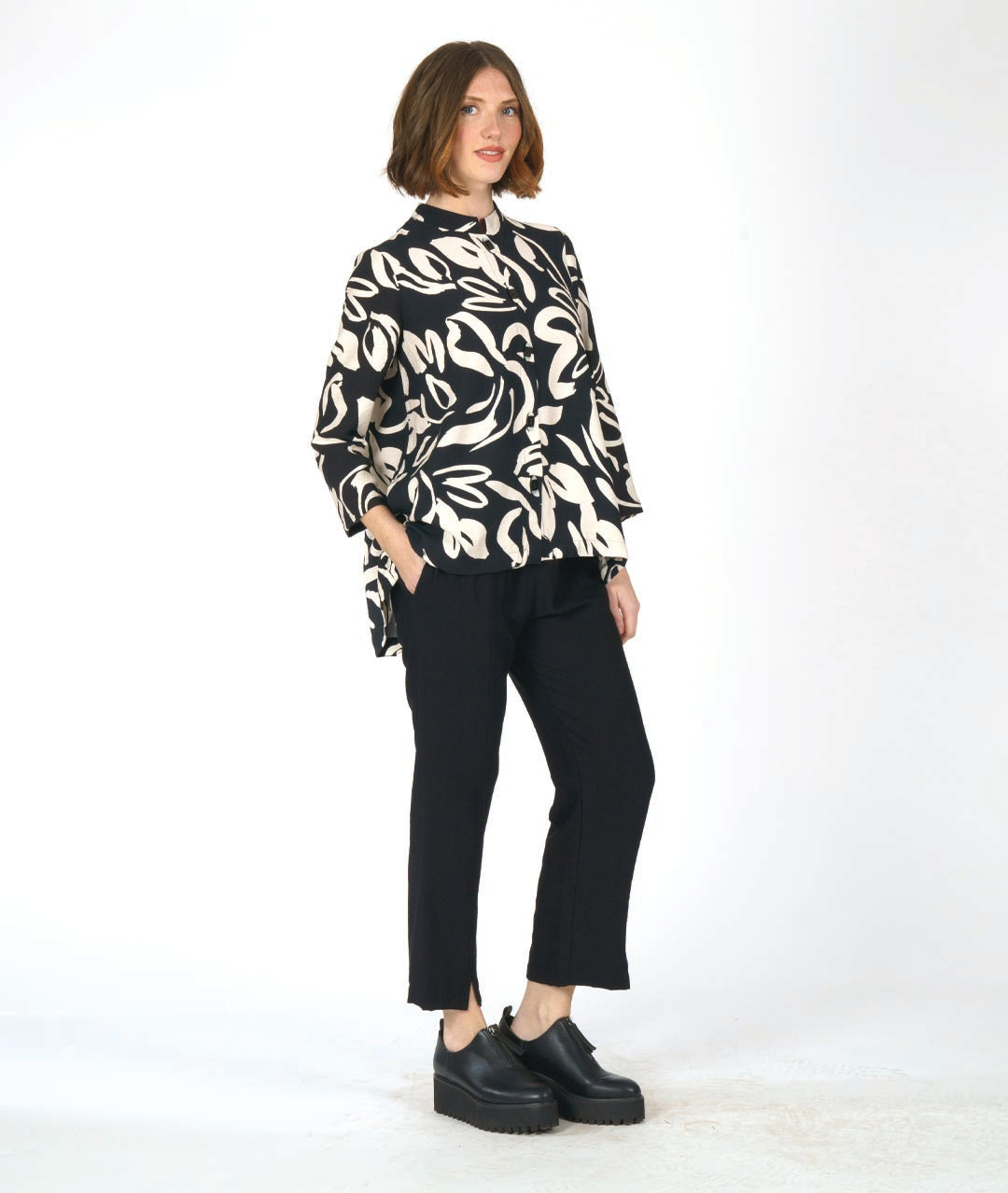 model in a straight cut black pant with a black and ivory floral print blouse with 3/4 sleeves, a mandarin style collar, and black and white buttons down the center front.