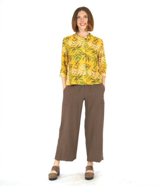 model in a straight leg brown pant with a yellow leaf print button down blouse. blouse has 3/4 sleeves, a boxy body and a twin button detail at the sleeves, back and front center