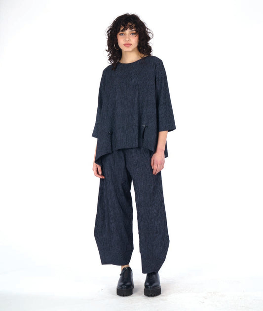 model in a grey and black pinstriped wide leg pant with a tapered ankle. worn with a matching pullover top with 3/4 sleeves and a dipped hem, princess seams and a double button detail above a small slit at the bottom of the princess seams