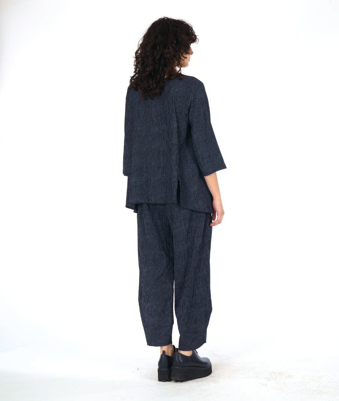 model in a grey and black pinstriped wide leg pant with a tapered ankle. worn with a matching pullover top with 3/4 sleeves and a dipped hem, princess seams and a double button detail above a small slit at the bottom of the princess seams