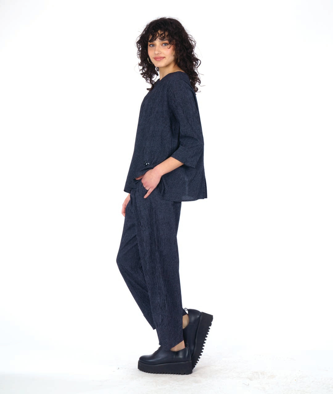 model in a grey and black pinstriped wide leg pant with a tapered ankle. worn with a matching pullover top with 3/4 sleeves and a dipped hem, princess seams and a double button detail above a small slit at the bottom of the princess seams