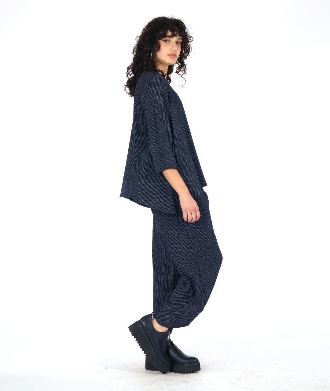 model in a grey and black pinstriped wide leg pant with a tapered ankle. worn with a matching pullover top with 3/4 sleeves and a dipped hem, princess seams and a double button detail above a small slit at the bottom of the princess seams