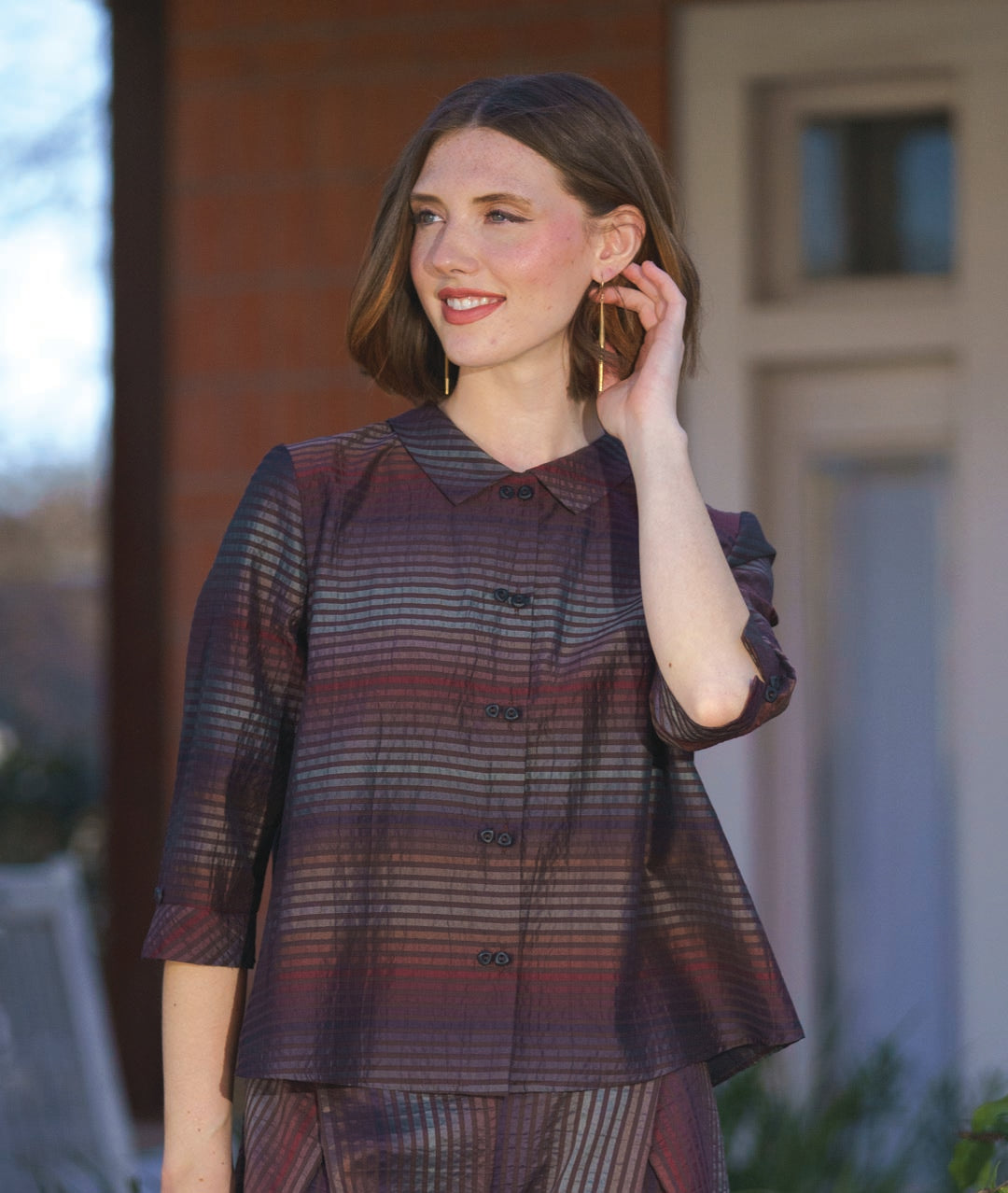 model in a boxy button down blouse in a brown and red tone stripe. worn with a matching wide leg pant that overlaps at each hip