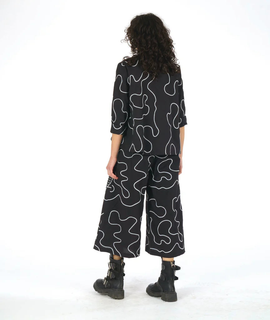 model showing back of matching black and white swirl and circle patterned top and wide leg pants against white background