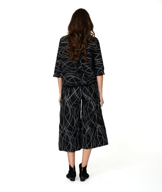 model in a wide leg black pant with a grey and blue embroidered stripe. worn with a matching button up blouse