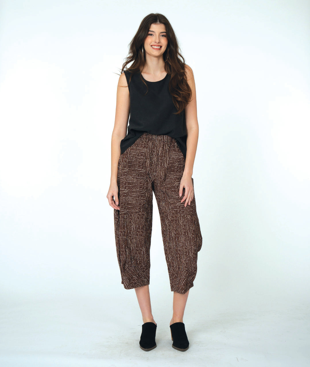Woman wearing a black sleeveless top and brown patterned pants on a white background