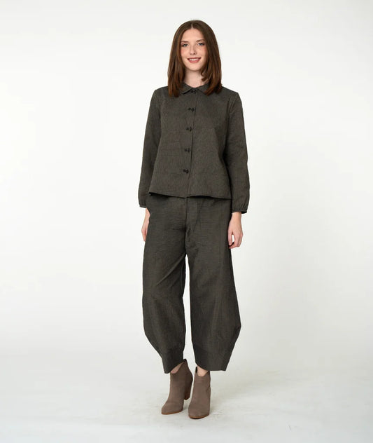 A woman modeling a dark olive green two-piece linen set consisting of a button-front top and matching wide-leg trousers, paired with brown ankle boots, against a plain white studio background.