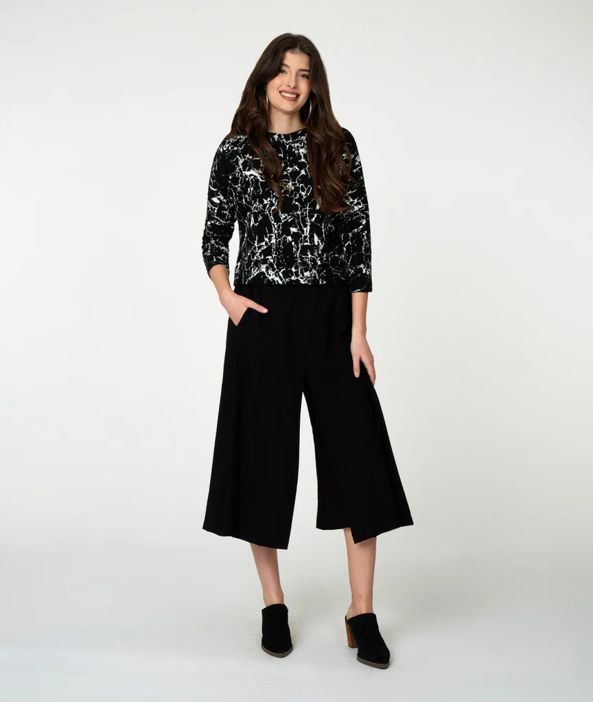Woman wearing a black and white marble patterned top with wide-leg black pants on a white background