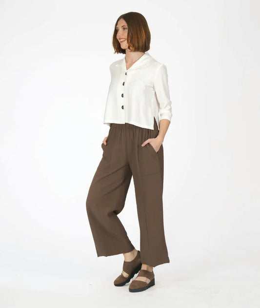 model wearing white button up 3/4 sleeve top with half circle buttons, paired with brown pants and shoes