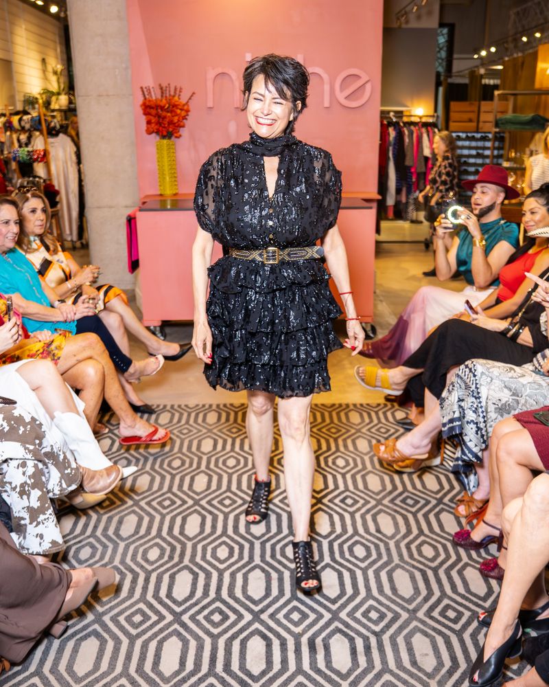 model in a black dress with neck tie and belt walking down runway