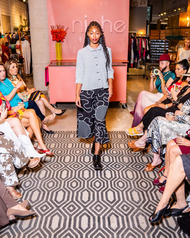 model posing in a checkered button up top and swirl pattern pants on a runway