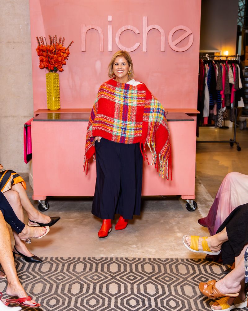 model wearing a red plaid poncho, navy pants and red boots on a runway