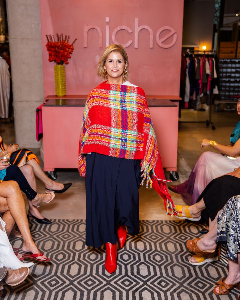 model wearing a red plaid poncho, navy pants and red boots on a runway