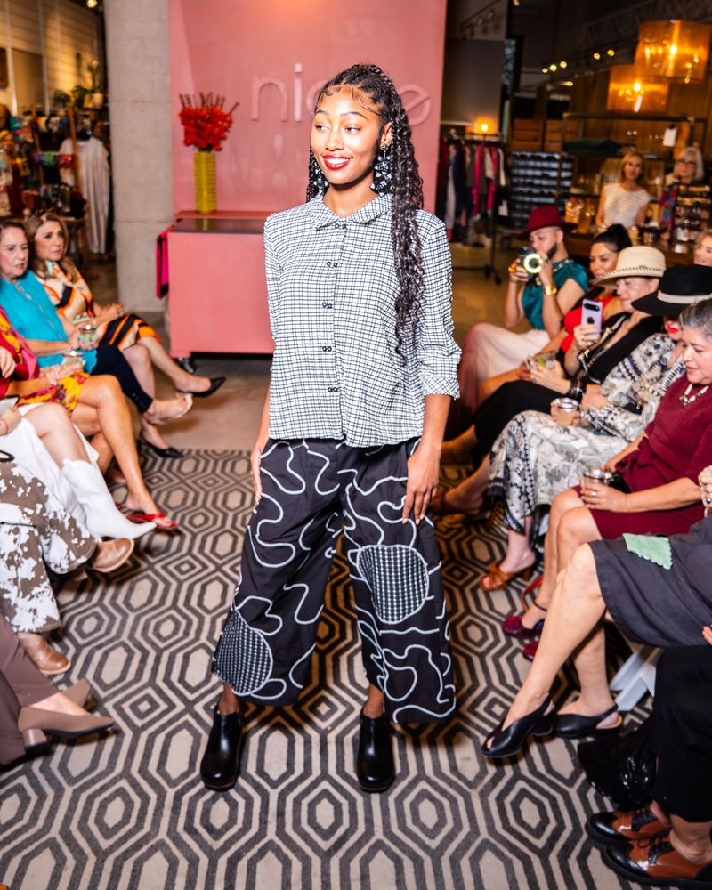 model posing in a checkered button up top and swirl pattern pants on a runway