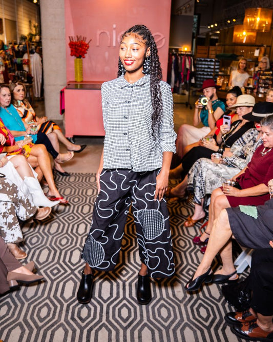 model posing in a checkered button up top and swirl pattern pants on a runway