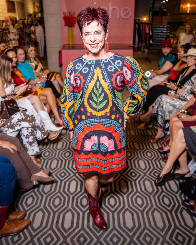 model in a colorful embroidered dress and red boots walking down runway