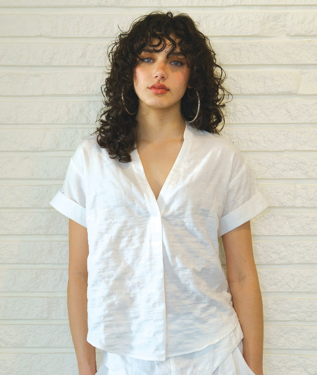 MODEL IN A WHITE TEXTURED SHIRT WITH A V-NECK, CUFFED SLEEVES AND A SMALL STANDING COLLAR