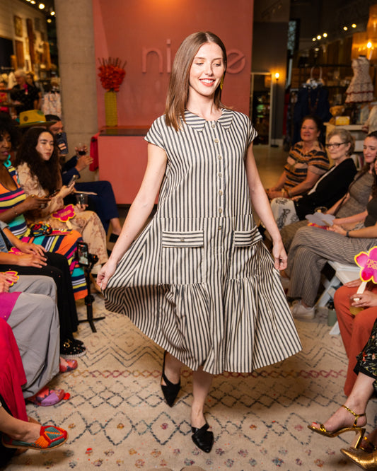 Woman in a black and white striped dress walking on a catwalk with an audience watching.
