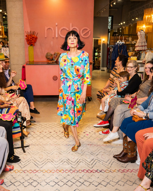 Woman in a colorful dress walking on a runway with 'niche' branding in the background.