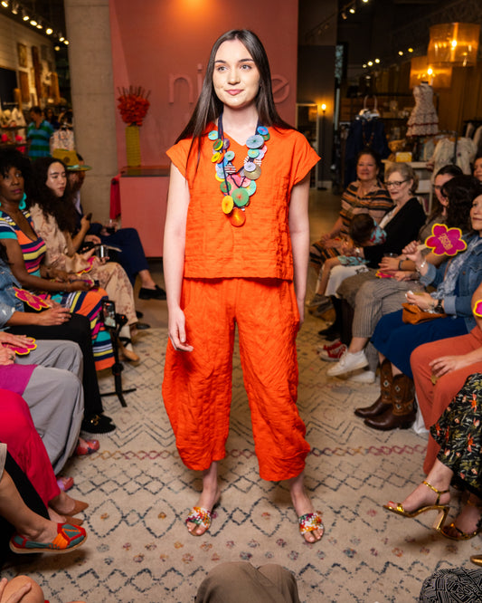Model wearing an orange set and pant with colorful necklace at a fashion event
