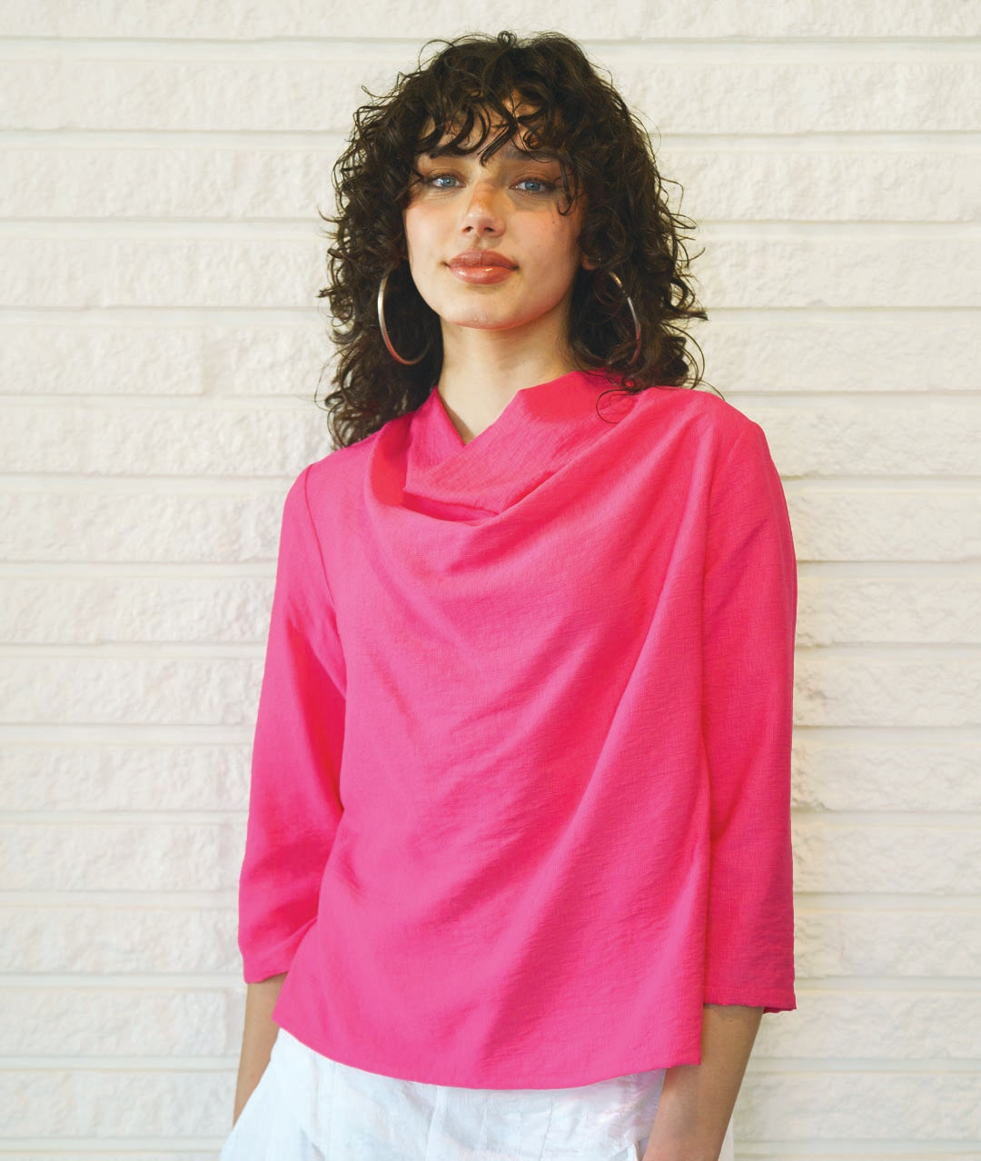 model in a white pant with a hot pink pullover top with 3/4 sleeves and a cowl neckline