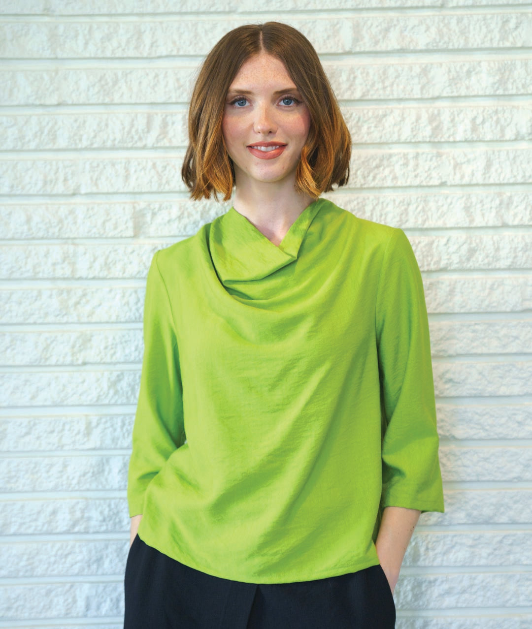 model in a black pant with a lime green pullover top with 3/4 sleeves and a cowl neckline