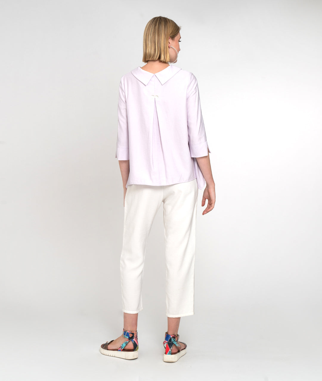 model in a light lilac button down blouse with 3/4 sleeves and a twin button detail. worn with a slim cut white pant with small slits at the ankle