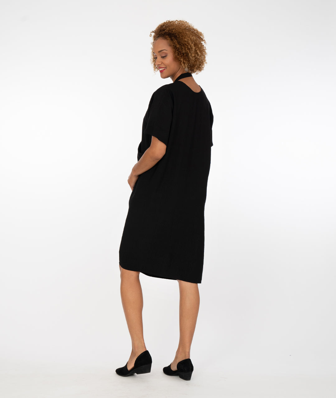 model in a black dress with a halter style strap at her neck in front of a white background