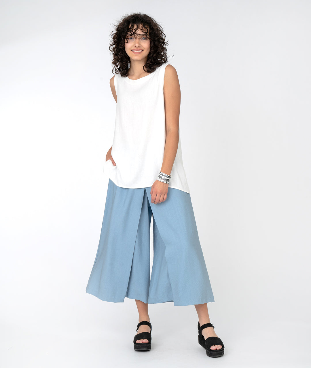 model in a long white tank with a wide leg light blue pant with an overlap panel in the front