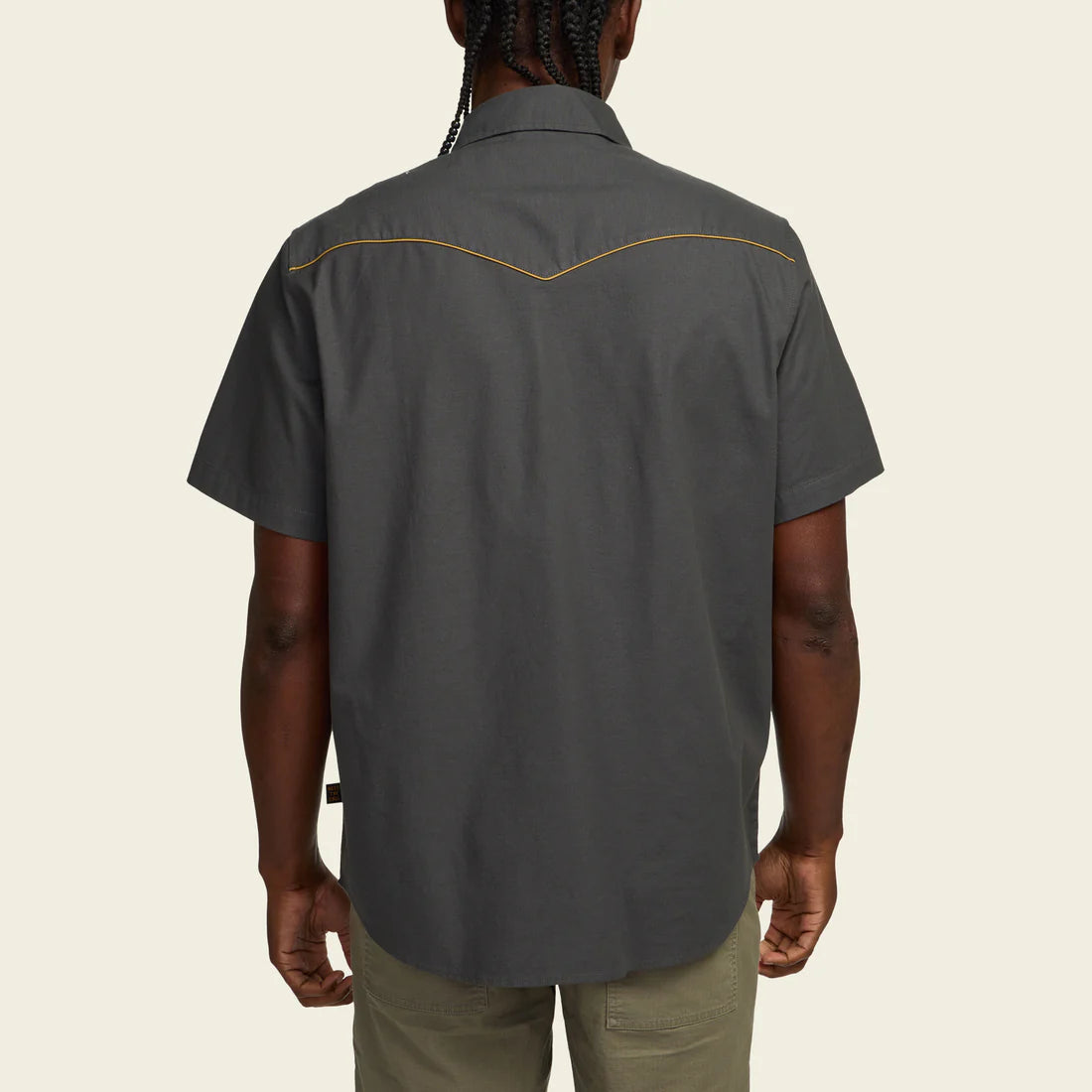 Person wearing a black short-sleeve shirt with yellow stitching on a beige background