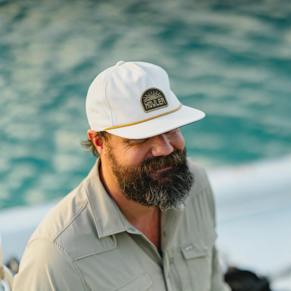 Man wearing a white cap with a logo, standing by a body of water.