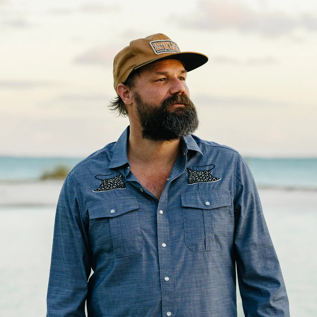 Man wearing a blue shirt and a brown cap, standing on a beach.
