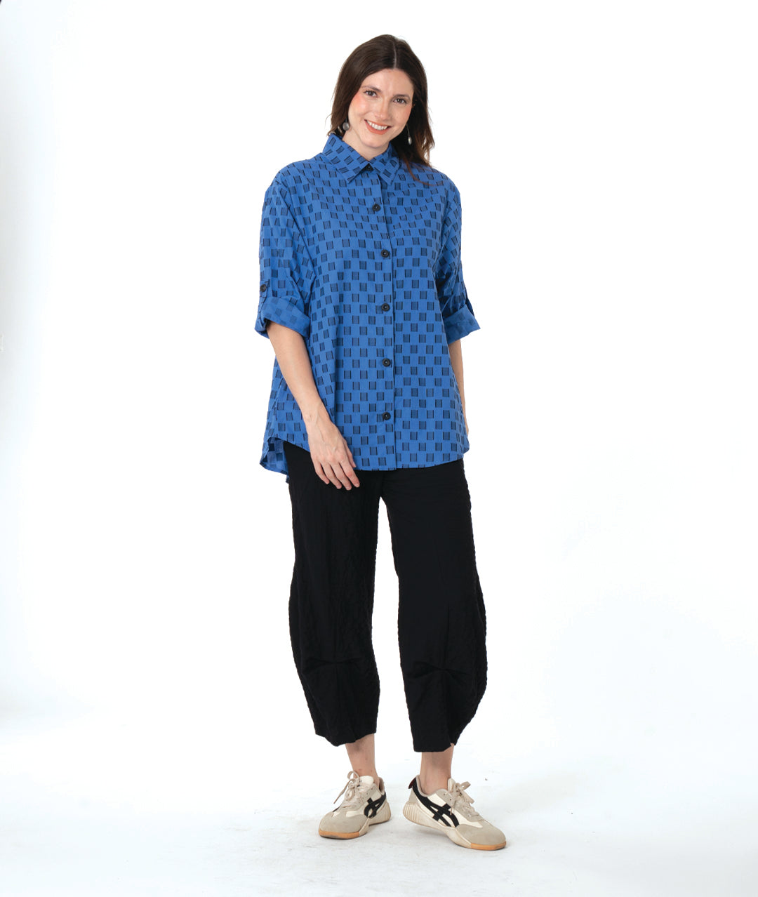 Woman wearing a blue and black checker board patterned blouse and black wide leg pants on a white background