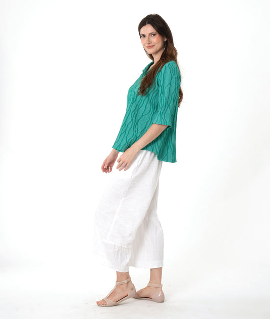 model in a white pant with a matching green textured pullover with an open collar, short sleeves and a curved hem