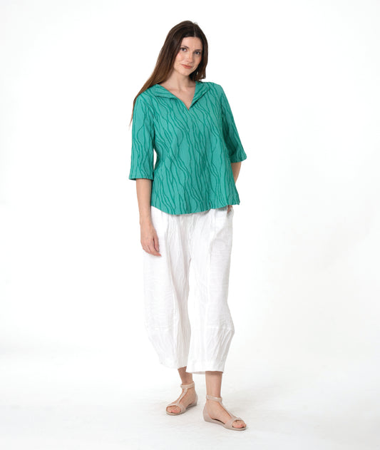 model in a white pant with a matching green textured pullover with an open collar, short sleeves and a curved hem