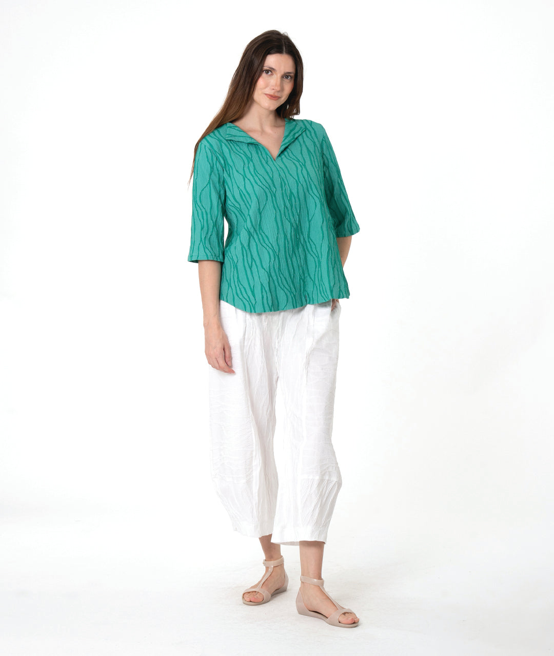 model in a white pant with a matching green textured pullover with an open collar, short sleeves and a curved hem