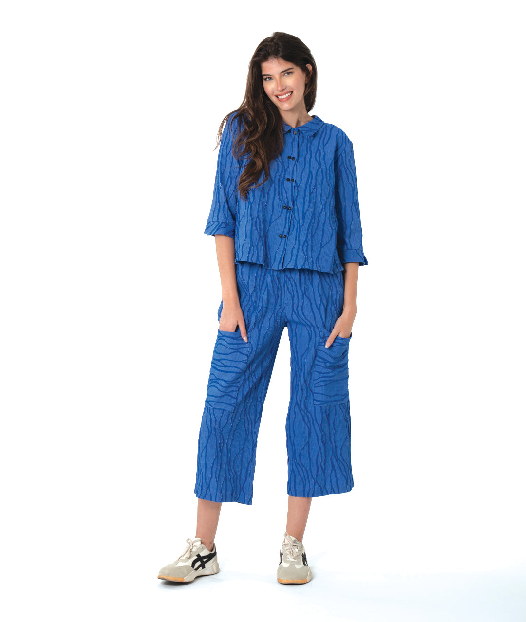 Woman wearing a blue textured pant and matching button down blouse on a white background