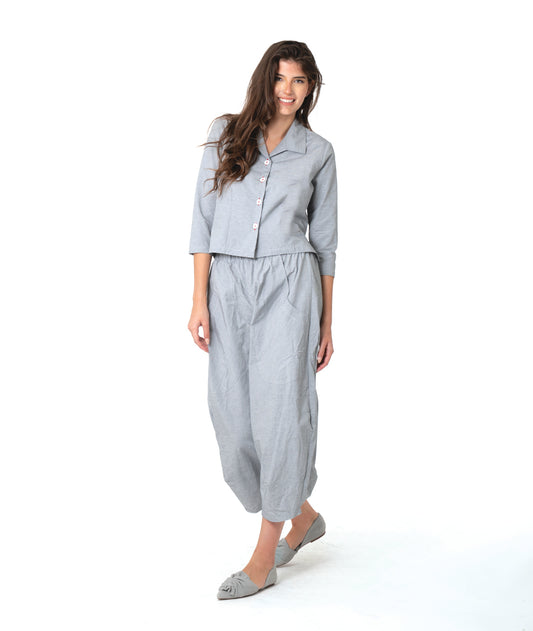 model in a grey and white pinstriped button down blouse with a short body, open collar, and contrasted red stitching at the buttons. worn with a matching wide leg pant