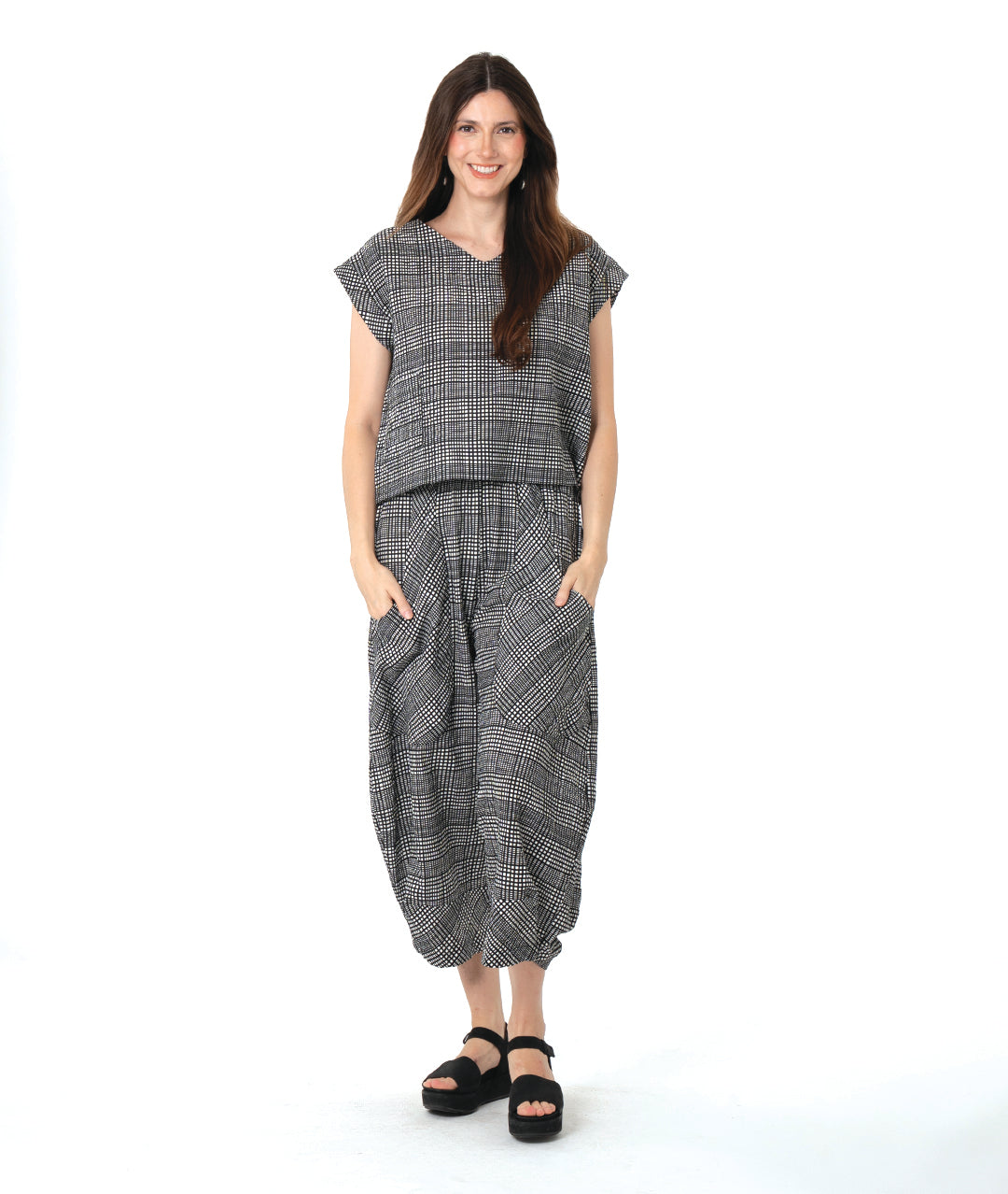 model in a black, white and grey plaid pair of pants with oversized contrasting pockets, wide legs and a tapered ankle. worn with a matching boxy pullover top
