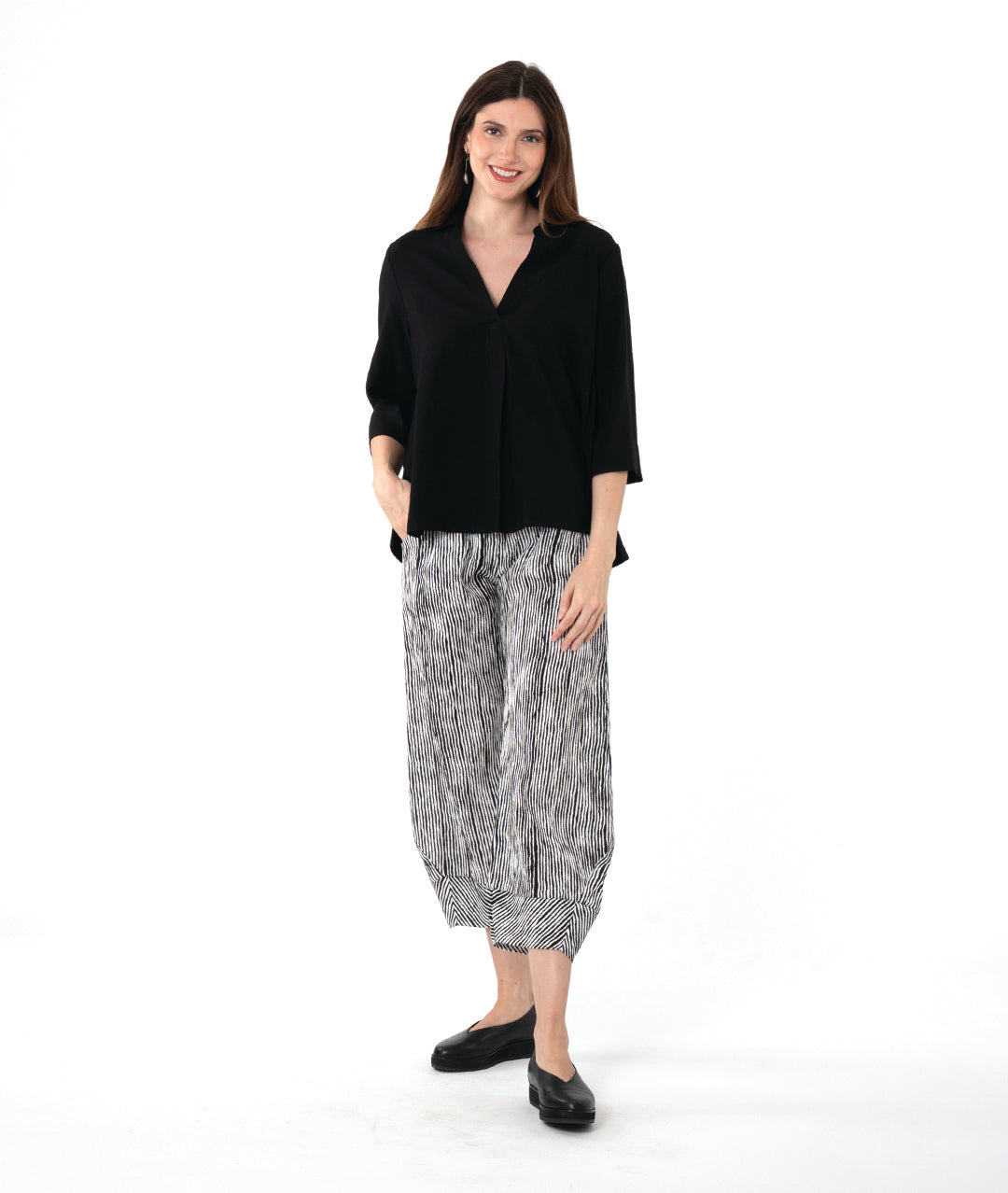 model in a wide leg black and white striped pant with a tapered ankle, worn with a black pullover blouse with 3/4 sleeves, side splits, a v-neck and open collar