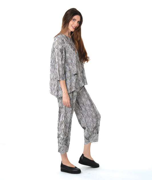 model in a wide leg black and white striped pant with a tapered ankle, worn with a matching pullover blouse with front splits and a double button detail