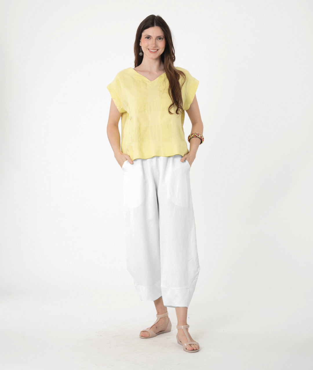 A woman modeling a light yellow short-sleeve linen top and white wide-leg linen pants against a plain white studio background.