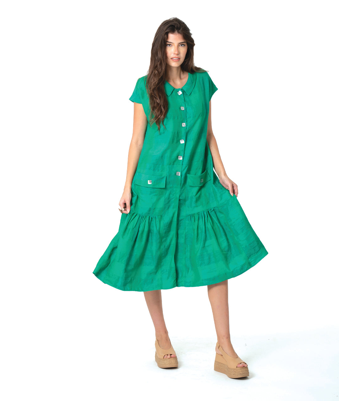A woman modeling a bright green short-sleeve midi dress with a button-down front, tiered skirt, and front pockets, paired with tan wedge sandals, against a plain white studio background.