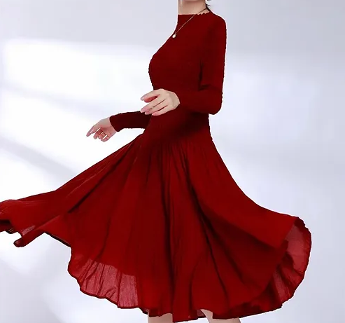 A woman wearing a red, scrunched, full-length dress with long sleeves, standing against a grey background.