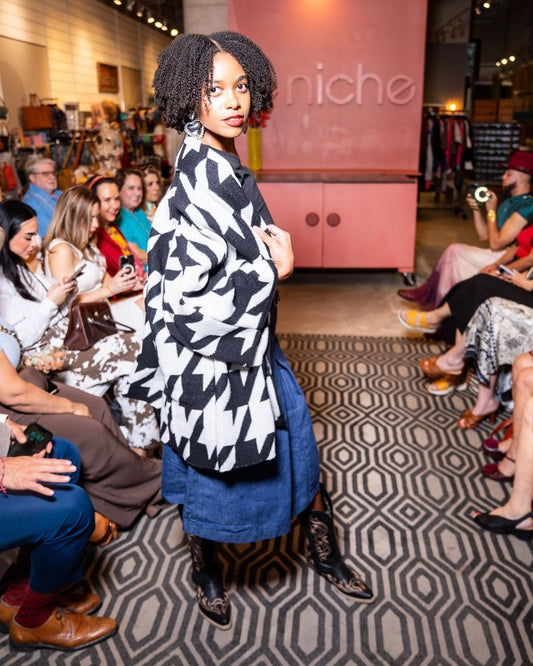 model wearing black and white houndstooth cardigan, black top, jean skirt and cowboy boots on a runway